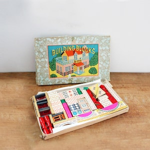 May include: Vintage "BUILDING BLOCKS" set with a colorful box featuring a house illustration. The open box reveals wooden blocks in various shapes and colors, including red, white, and green. A classic toy for creative play.