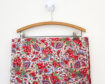 May include: A white fabric with a paisley pattern in red, blue, and green. The fabric is hanging on a wooden hanger.