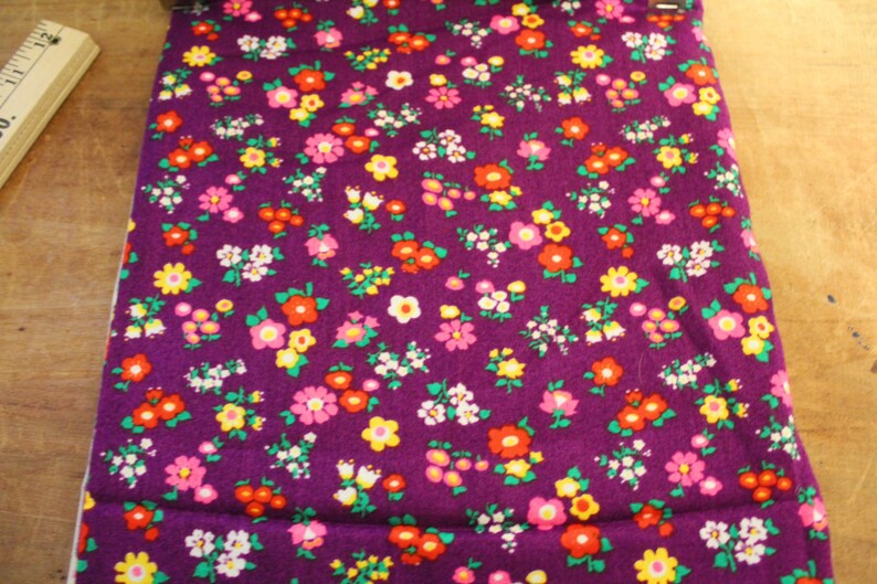 May include: Purple fabric with a repeating pattern of small pink, yellow, and orange flowers.