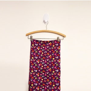 May include: A purple skirt with a floral print hanging on a wooden hanger. The skirt has a small floral pattern in shades of red, yellow, white, and green.