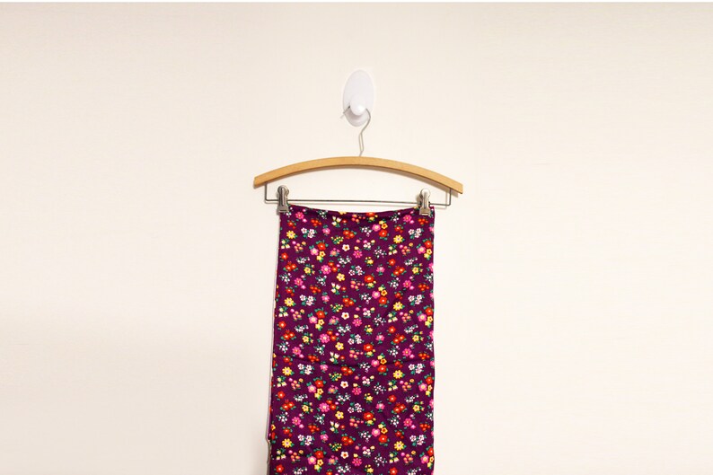 May include: A purple skirt with a floral print hanging on a wooden hanger. The skirt has a small floral pattern in shades of red, yellow, white, and green.
