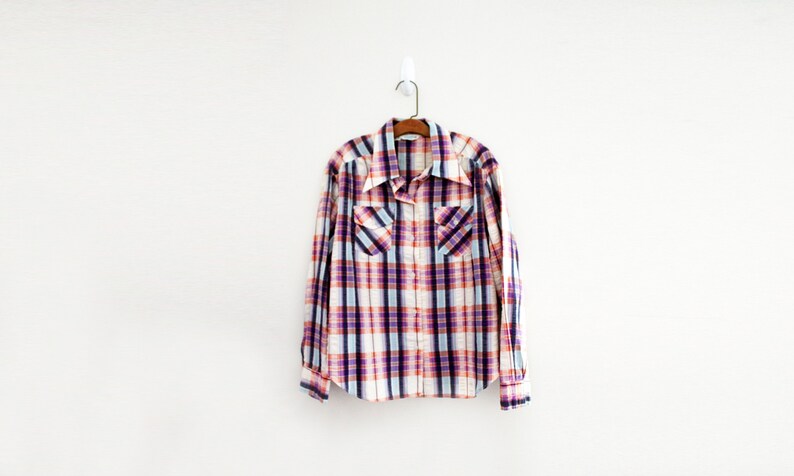 May include: A plaid shirt with a white background and red, blue, and purple checks. The shirt has a button-down collar and long sleeves.