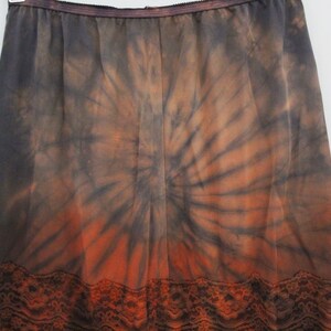 May include: A tie-dye skirt in shades of black, orange, and brown. The skirt features a spiral pattern and a lace trim at the hem. The elastic waistband is visible at the top.