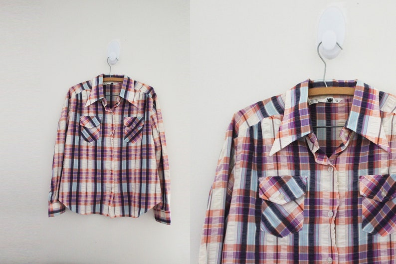 May include: A long-sleeved plaid shirt with a button-down collar. The shirt has a white, pink, purple, and blue plaid pattern. The shirt has two chest pockets.