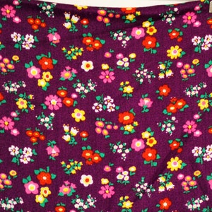 May include: Purple fabric with a small floral print featuring red, pink, yellow, and white flowers.