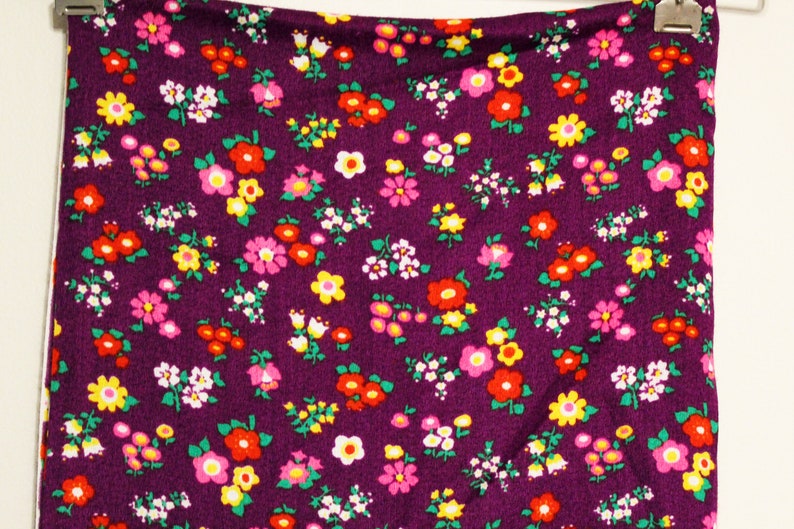 May include: Purple fabric with a small floral print featuring red, pink, yellow, and white flowers.