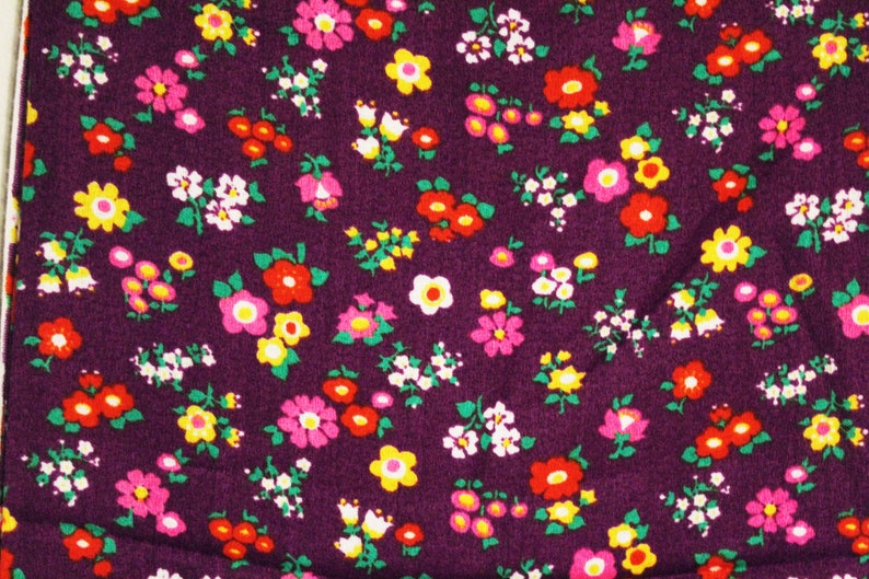 May include: Purple fabric with a repeating pattern of small pink, yellow, and red flowers.