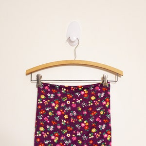 May include: A purple skirt with a small floral print hangs on a wooden hanger. The skirt has a waistband and is made of a soft, stretchy fabric.