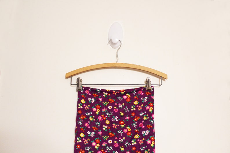 May include: A purple skirt with a small floral print hangs on a wooden hanger. The skirt has a waistband and is made of a soft, stretchy fabric.