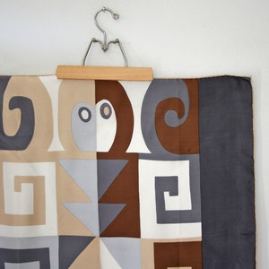 May include: A brown, gray, and white geometric patterned silk scarf hanging on a wooden hanger.