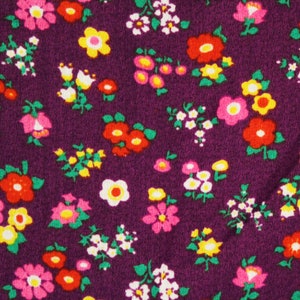 May include: Purple fabric with a repeating pattern of small, colorful flowers. The flowers are in shades of pink, red, yellow, and white.