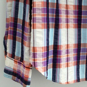 May include: A long-sleeved button-down shirt with a plaid pattern in shades of orange, blue, purple, and white.