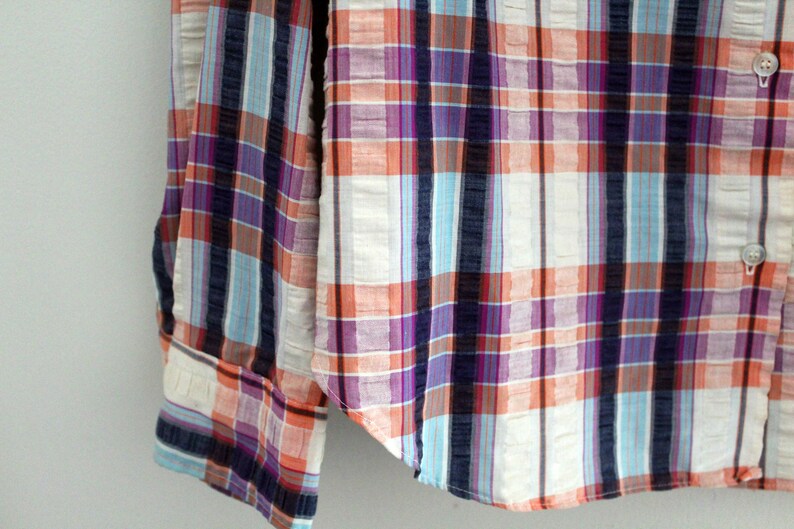May include: A long-sleeved button-down shirt with a plaid pattern in shades of orange, blue, purple, and white.