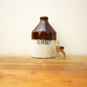 May include: A brown and white ceramic jug with the word "DECOR" printed on the side. A small gold deer figurine is in front of the jug.