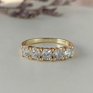 Könnte beinhalten: Ein Goldring mit fünf klaren runden Edelsteinen, die in einer Reihe angeordnet sind.