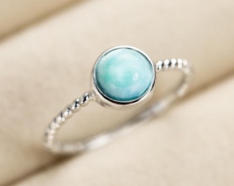 May include: A silver ring with a light blue gemstone. The ring has a beaded band.