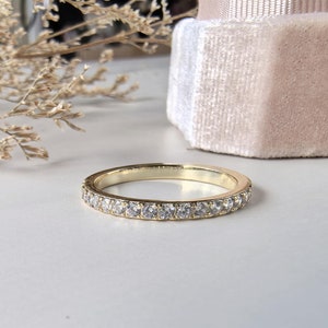 May include: A thin gold band with a row of small, clear diamonds set in a pave setting.
