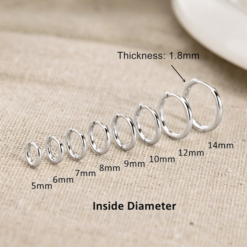 May include: A set of eight silver-toned hoop earrings arranged in a row by size. The earrings range from 5mm to 14mm in inside diameter, with a labelled thickness of 1.8mm. The text labels indicate the inside diameter for each individual hoop.