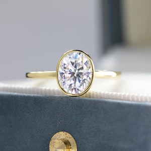 May include: A gold engagement ring with a bezel-set oval-shaped diamond.