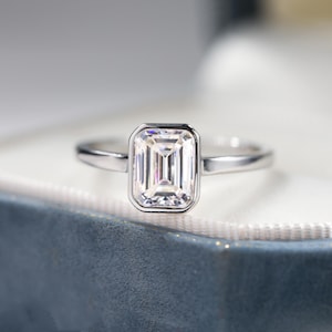 May include: A silver ring with a square-shaped, clear emerald-cut gemstone.