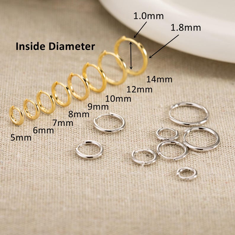 May include: A collection of gold and silver hoop earrings arranged by size. The gold hoops are lined up with labels from 5mm to 14mm. The text Inside Diameter, 1.0mm, and 1.8mm indicates the thickness and measurement of the hoops.