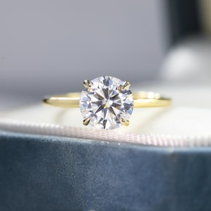 Puede incluir: Un anillo de compromiso de oro con un gran diamante redondo y claro.