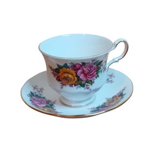 May include: A white teacup and saucer set with a floral design. The cup and saucer have a gold trim and feature a pink, yellow, and green floral pattern.