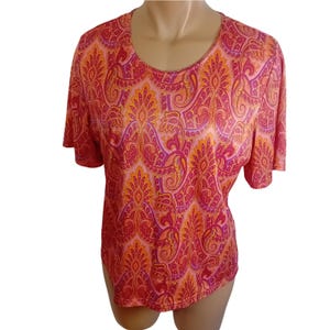 May include: A short-sleeved top with a vibrant paisley pattern in shades of red, orange, and purple. The top has a scoop neckline and a loose, flowing fit. The fabric appears to be lightweight and suitable for warm weather.