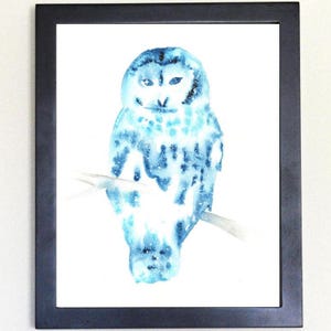 May include: Framed watercolor painting of an owl in shades of blue. The owl is perched on a branch against a white background. The artwork is enclosed in a black frame, suitable for wall decor.