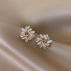 Peut inclure: Une paire de boucles d'oreilles en or avec des pierres blanches ressemblant à des opales disposées en forme de feuilles.