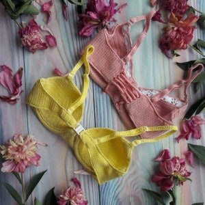 May include: Two crocheted tops, one yellow and one pink, laid out on a wooden surface with pink flowers.