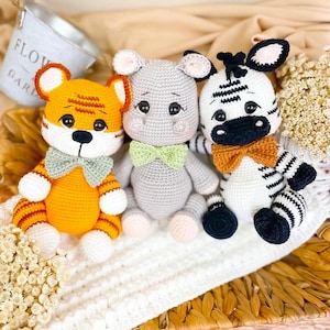 May include: Three crocheted stuffed animals: a tiger with orange and black stripes, a gray hippo with a green bow tie, and a black and white zebra with an orange bow tie.
