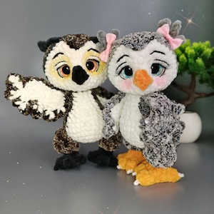 May include: Two handmade crochet owls. One owl is brown, white, and black with large orange eyes and a wing extended. The other owl is gray, white, and black with a pink bow and orange beak. Both have yellow and orange feet.
