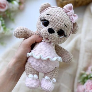 Peut inclure: Poupée ours en peluche crochetée de couleur marron clair, vêtue d'une tenue rose avec des bordures blanches et des chaussures assorties. L'ours a de grands yeux expressifs, de longs cils et un nœud rose sur la tête. La poupée est faite à la main.