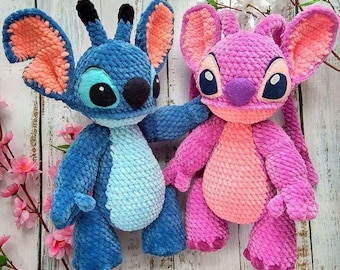 May include: Two handmade crochet plush toys, one blue and one pink, resembling cartoon characters. The blue toy has large ears with orange insides, and the pink toy has a similar design. Both have large eyes and are made of soft, textured yarn.