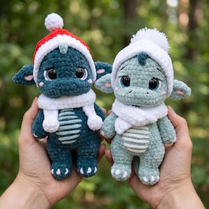 May include: Two plush dragon toys made of soft yarn. The left dragon is dark teal with a red and white Santa hat and white scarf. The right dragon is light sage green with a white winter hat and white scarf. Both have large black eyes.
