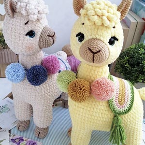 May include: Two crocheted llama toys, one beige and one yellow, with colourful pom-poms around their necks. The yellow llama has a green and rainbow striped scarf.