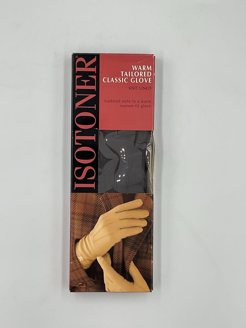 May include: A rectangular product box for Isotoner warm tailored classic gloves. The packaging features the brand name in large vertical black text, a red header with white text, and an image of tan gloves against a brown plaid fabric.