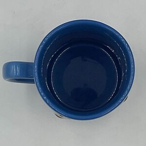 May include: A top-down view of a ceramic mug featuring a deep blue interior and a matching blue handle. The rim of the mug is circular, and the smooth, glossy finish of the blue glaze is visible throughout the inside and on the exterior handle.