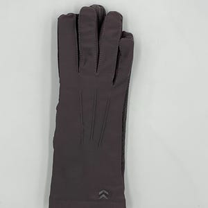 May include: A pair of dark gray gloves featuring a smooth, solid-colored fabric finish. The gloves have three vertical stitched lines on the back of the hand and a small, reflective chevron-shaped logo detail near the wrist opening.