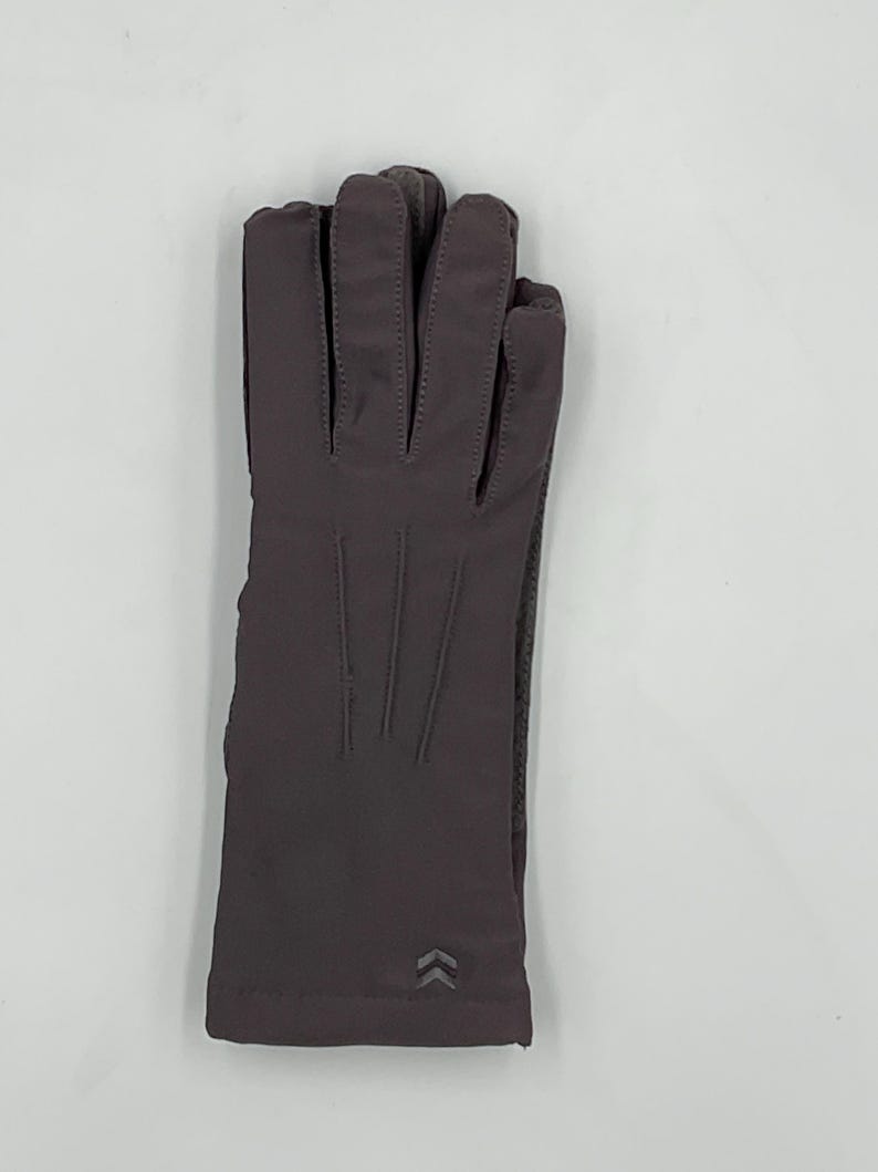 May include: A pair of dark gray gloves featuring a smooth, solid-colored fabric finish. The gloves have three vertical stitched lines on the back of the hand and a small, reflective chevron-shaped logo detail near the wrist opening.