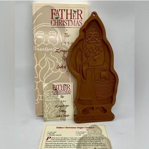 Puede incluir: Un molde para galletas de cerámica marrón con forma de Papá Noel sosteniendo una cesta, acompañado de una caja y una tarjeta de receta etiquetada como Father Christmas The 1990 Longaberger Pottery Cookie Mold. El molde presenta una figura en relieve.