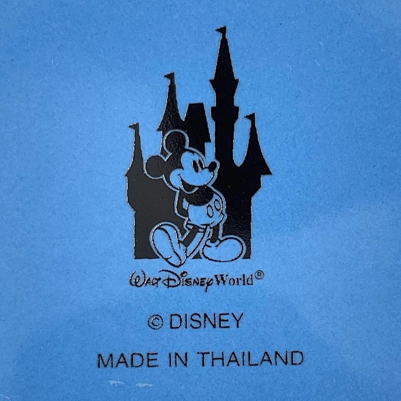 May include: A light blue surface featuring a black silhouette of the Cinderella Castle with Mickey Mouse standing in front. Below the graphic, the text reads Walt Disney World, followed by the copyright symbol, DISNEY, and MADE IN THAILAND.