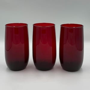 Könnte beinhalten: Drei Weingläser ohne Stiel in tiefroter Farbe. Die Gläser haben einen abgerundeten Boden, der sich nach oben hin verjüngt. Die Farbe dunkelt sich zum Boden hin ab und erzeugt einen subtilen Farbverlauf. Die Gläser sind gleichmäßig vor einem weißen Hintergrund angeordnet.