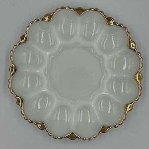 May include: A white, scalloped-edge serving dish with a gold-colored trim. The dish has a central circular area surrounded by twelve individual compartments, perfect for serving appetizers or condiments. The dish is made of a glossy, opaque material.