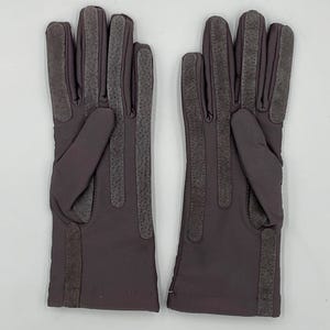 May include: A pair of dark mauve gloves featuring textured, darker mauve panels running vertically along the fingers and the outer edge of the palm. The gloves have a smooth, matte finish on the main body and a simple, straight-cut wrist opening.