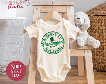 May include: A white baby onesie with a green shamrock and a leprechaun hat design. The text reads "Prone to Shenanigans and Malarkey".