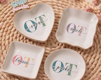 May include: Four white ceramic trinket dishes in different shapes: heart, square, round, and a scalloped square. Each dish has a gold rim and features a name and the letters "OT" in various colors. The text "SHIP from USA" is in the upper left corner.
