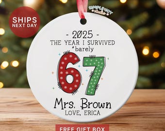 May include: A white ceramic Christmas ornament with a red ribbon. The ornament features the text "- 2025 - THE YEAR I SURVIVED *barely" and the number "67" in red and green. The ornament is personalized with "Mrs. Brown LOVE, ERICA".