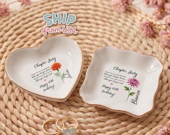 May include: Two white ceramic trinket dishes, one heart-shaped and one square with scalloped edges, both featuring gold rims. Each dish displays the text Chapter Sixty, Happy 60th Birthday, and a floral illustration with a name, Julia or Bianca.